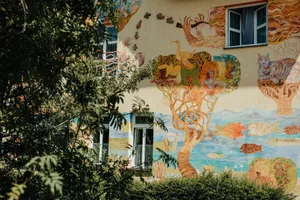 Vibrant mural depicting whimsical scenes on a residential building wall surrounded by greenery. jigsaw puzzle