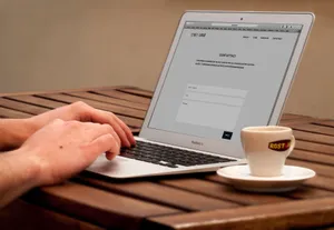 Close-up of hands typing on a laptop next to a cup of coffee on a wooden desk. jigsaw puzzle