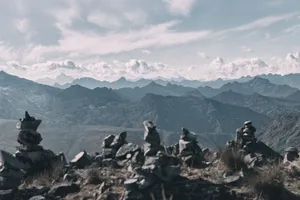 Serene view of rock cairns stacked against a vast mountain range with cloudy skies. jigsaw puzzle