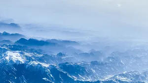 A stunning aerial view of snow-capped mountains enveloped in mist and fog. jigsaw puzzle