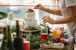 Crop anonymous female chef in casual clothes standing at table with various dishes and drinks and putting berries on top of delicious cake jigsaw puzzle