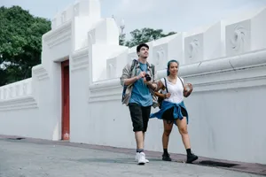 Young tourists exploring a city, walking by a historic white wall on a bright day. jigsaw puzzle
