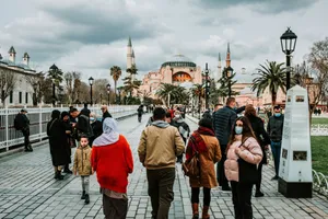 Pedestrians in warm clothes and masks walking on cobblestone pavement with lanterns and palm trees against aged mosque jigsaw puzzle