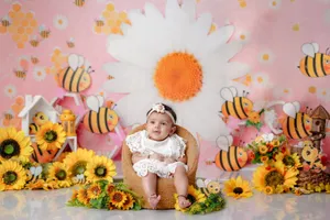 Cute baby girl in white dress sits among bright sunflowers and bees, creating a cheerful spring atmosphere. jigsaw puzzle