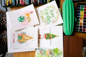 Top view of handmade Christmas cards with artistic designs on a wooden table surrounded by art supplies. jigsaw puzzle