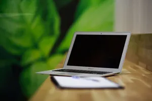 A sleek silver laptop sits open on a wooden desk with a green backdrop, illustrating a modern workspace. jigsaw puzzle