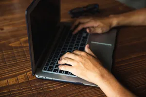 From above crop faceless male using contemporary netbook with black screen and typing on keyboard while sitting at wooden table jigsaw puzzle