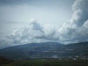 Breathtaking view of a cloudy sky over a lush green valley with distant wind turbines. jigsaw puzzle
