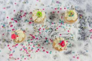 Overhead view of cupcakes with vibrant icing and decorative sprinkles on a snowy surface. jigsaw puzzle