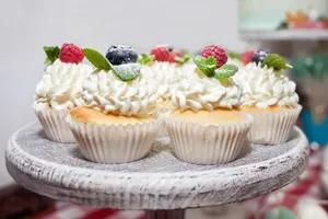 Delicious sweet cupcakes decorated with cream and mint leaves and blueberries and raspberries on table in light room jigsaw puzzle
