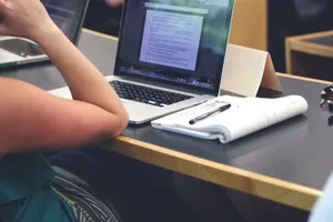 A student in a classroom setting using a laptop and taking notes in a notebook. jigsaw puzzle