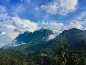 Stunning view of mountain range with lush greenery and dramatic clouds against a vibrant blue sky. jigsaw puzzle