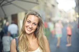 Portrait of a smiling woman with blonde hair standing outdoors in a bustling street setting. jigsaw puzzle