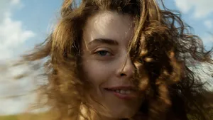 A beautiful close-up portrait of a smiling young woman with flowing curly hair against a sunny sky. jigsaw puzzle