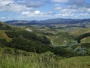 Expansive landscape of lush rolling hills and valleys under a cloudy blue sky. jigsaw puzzle