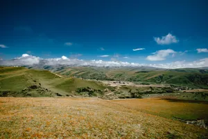 Sprawling green mountains with a clear blue sky and scattered clouds creating a peaceful natural scene. jigsaw puzzle