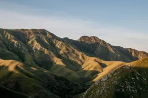A breathtaking view of rolling mountains bathed in golden light under a clear sky. jigsaw puzzle