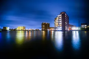 A vibrant cityscape featuring illuminated buildings reflecting on a calm river at night. jigsaw puzzle