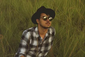 A stylish young man in a plaid shirt and hat enjoying a sunny day in a green field. jigsaw puzzle
